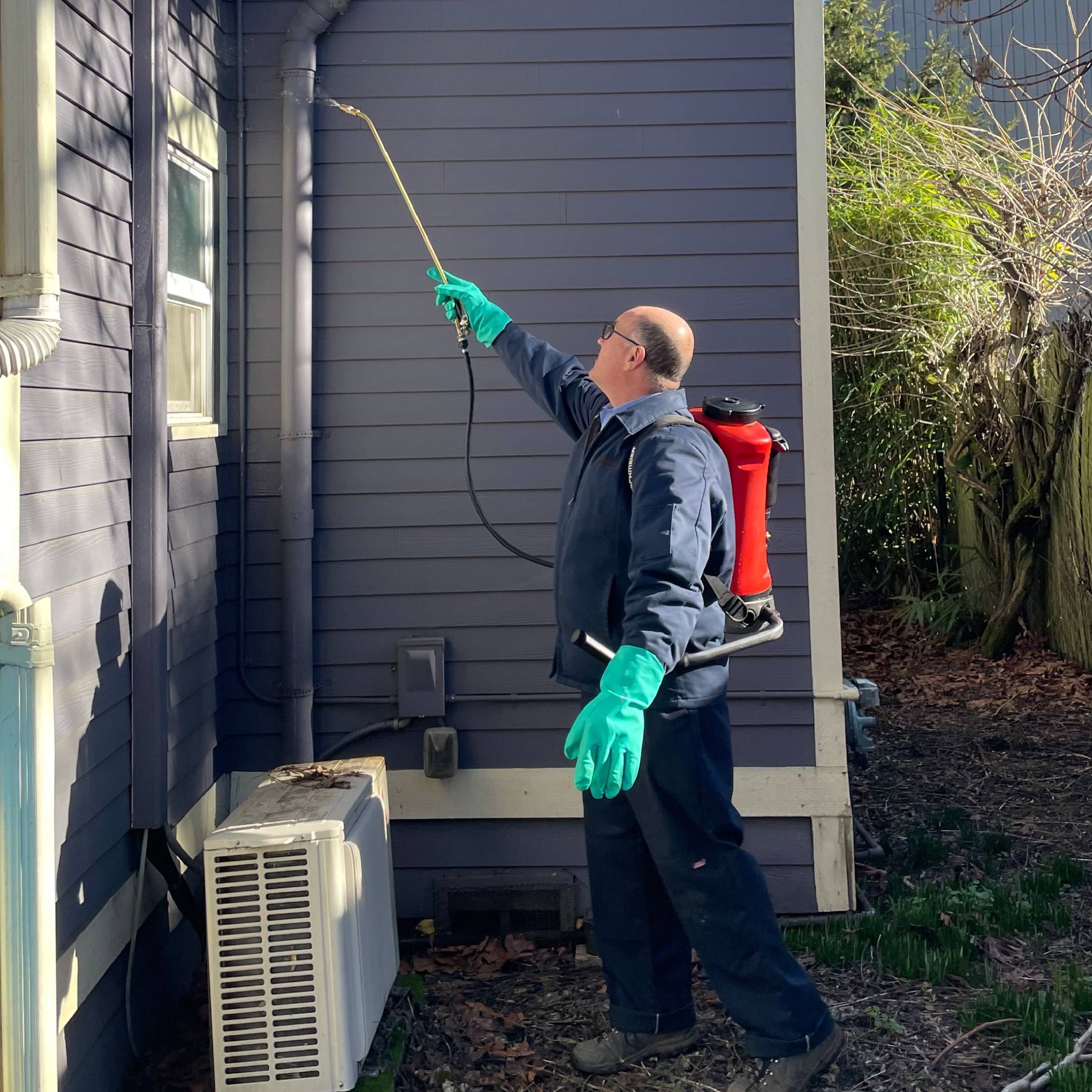 Lonnie spraying pest control treatment around a house